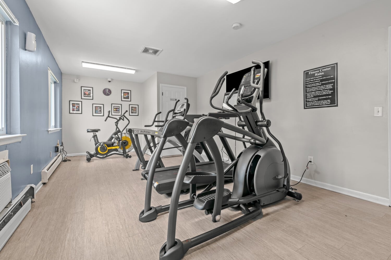 Elliptical machines and stationary bike in a well-lit fitness room with framed wall art.