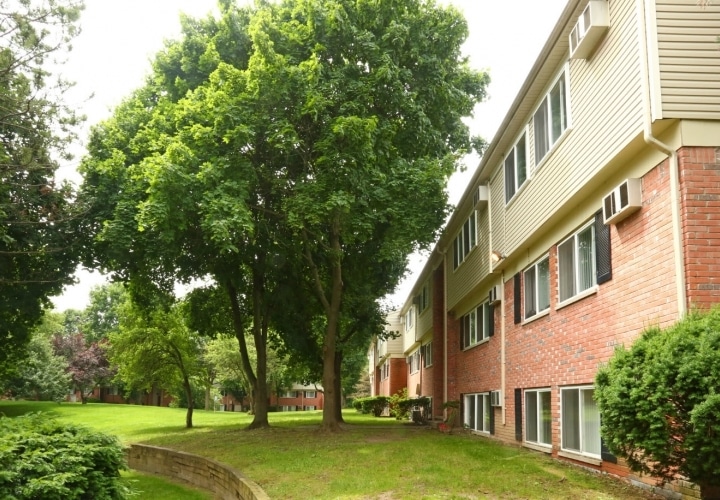 Apartment building with trees and a lush green lawn on a sunny day.